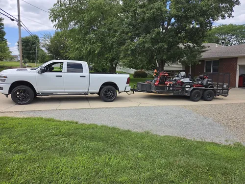 Pickup and trailer loaded with zero turn mowers parked in a residential driveway