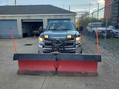 Pickup fitted with a red snow plow blade parked at the shop